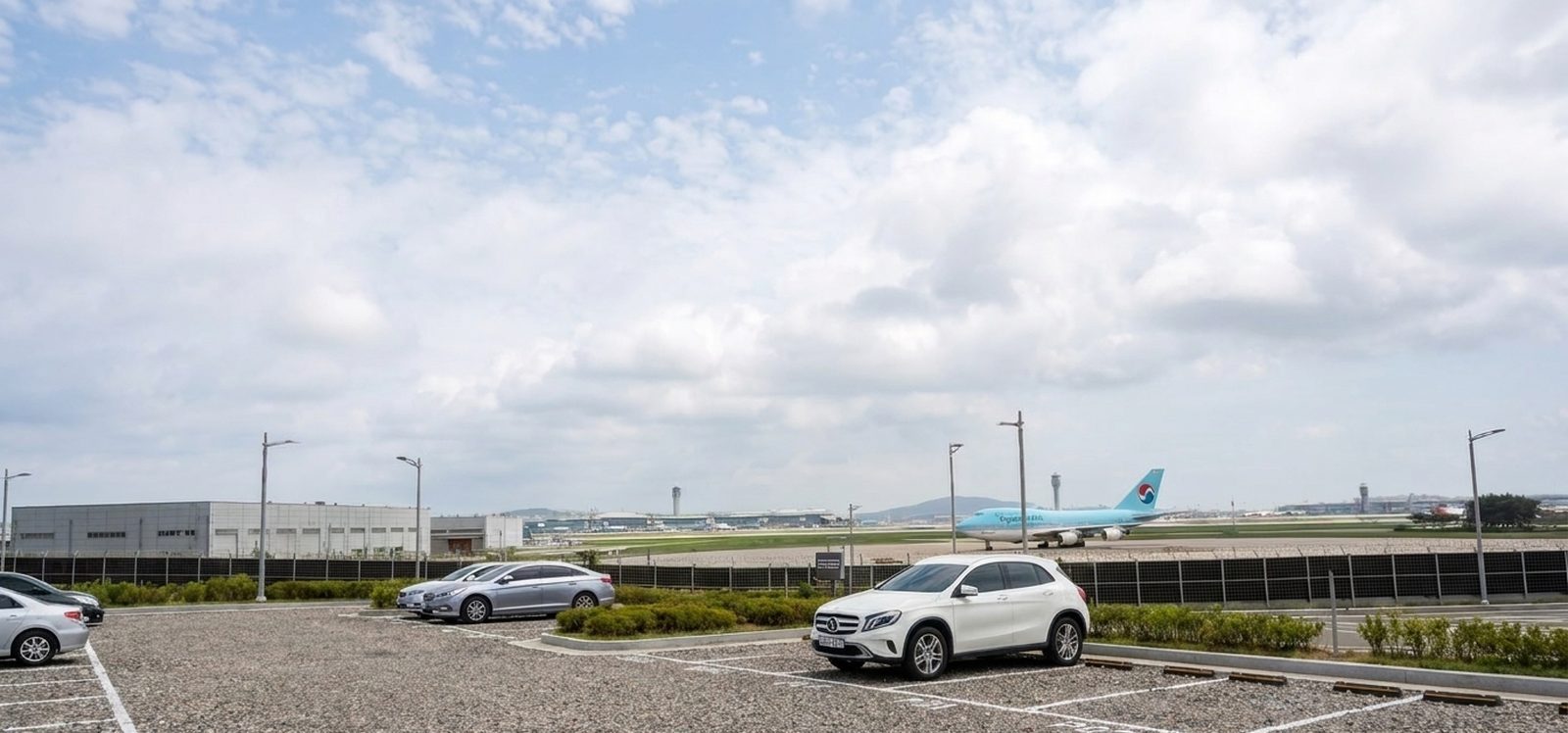 인천공항 활주로 옆 포시즌 파쇄석 주차장 전경 — 주차 차량과 유도로의 항공기